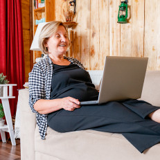 Nainen käyttää kannettavaa tietokonetta sohvalla loikoillen.